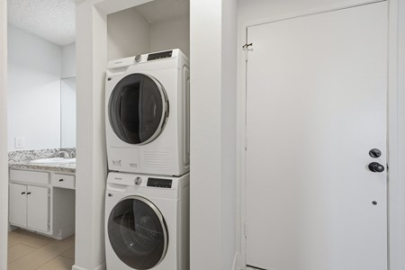A white door is on the right of a stack of two white washing machines.