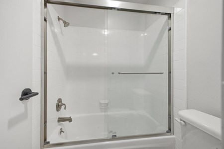 A white bathroom with a glass shower door and a white tub.
