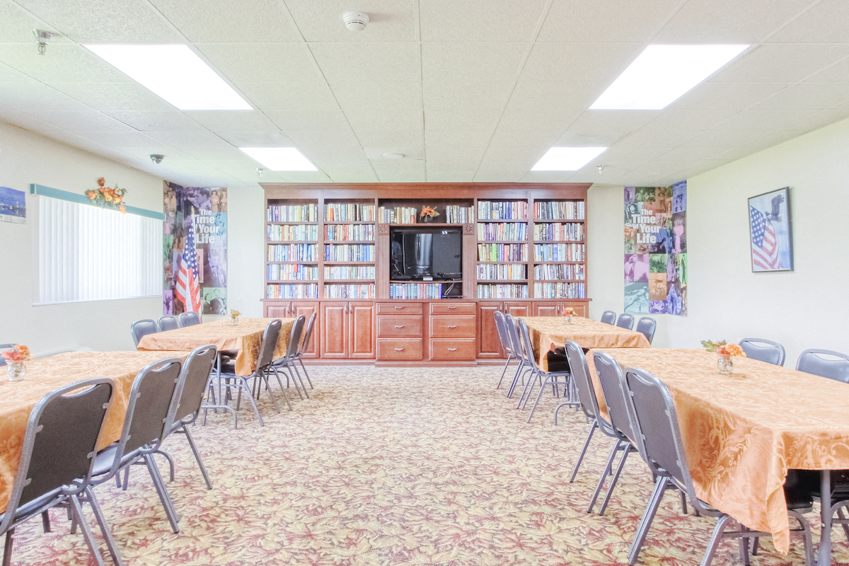large community room with tables, chairs, TV, and many shelves of books