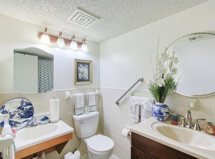 bathroom with grab bars, toilet, two sink vanities, and ample lighting