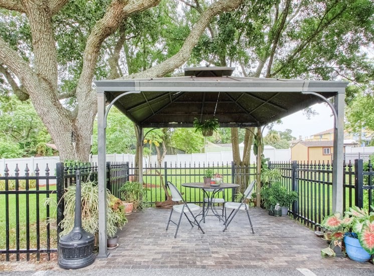 outdoor pavillion with seating under a canopy beside iron fence with potted plants