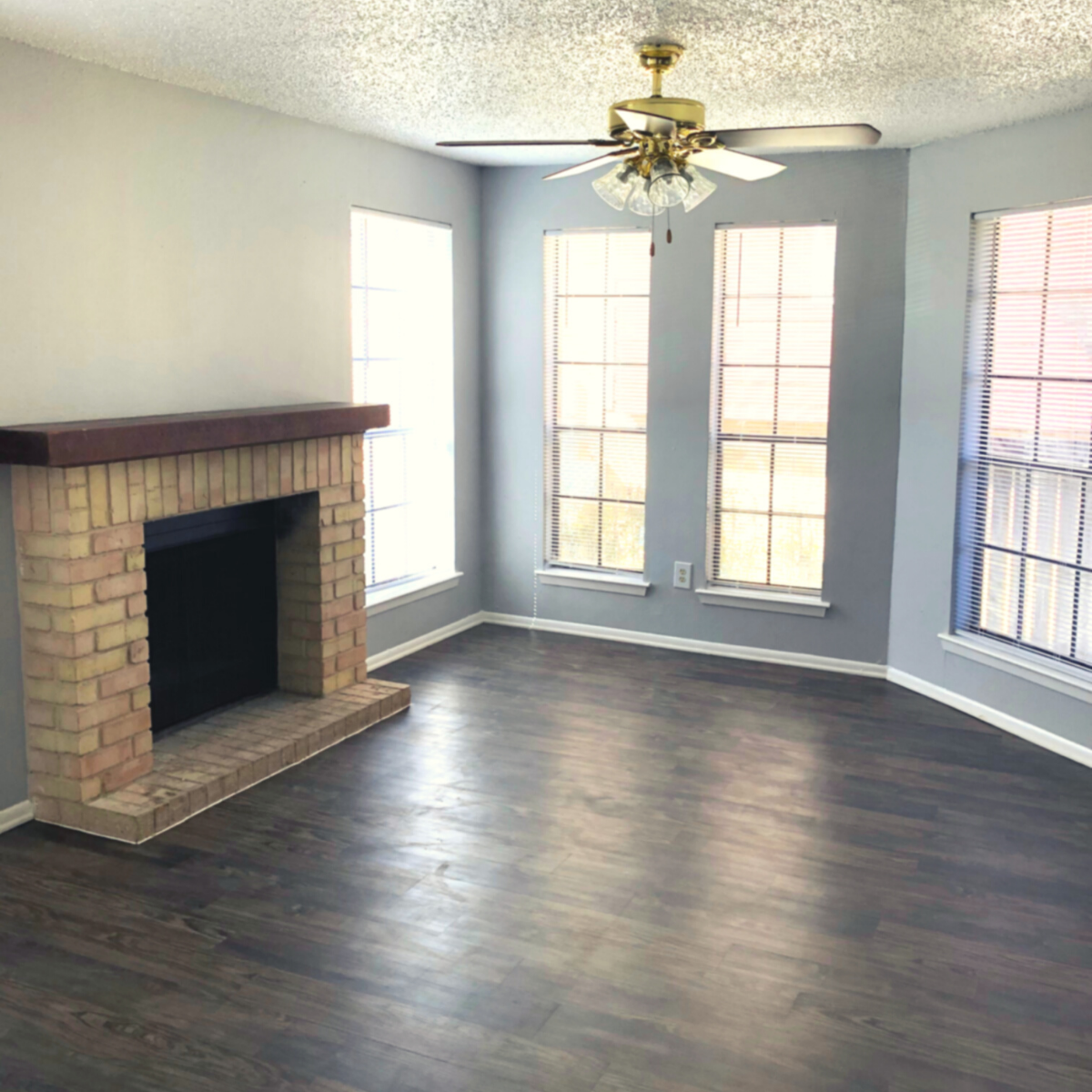 Living room with dark wood floors, brick fireplace with cherrywood mantle, and 4 wall length mirrors