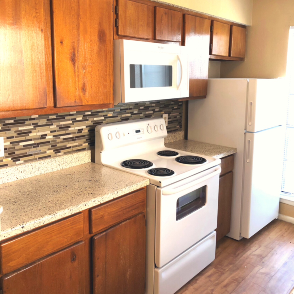 Sunlit kitchen with multicolored tile back splash, white appliances, and light cherrywood cabinets