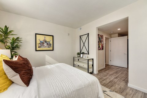 Master bedroom with large bed,  dresser/table, wall art and hardwood inspired flooring.