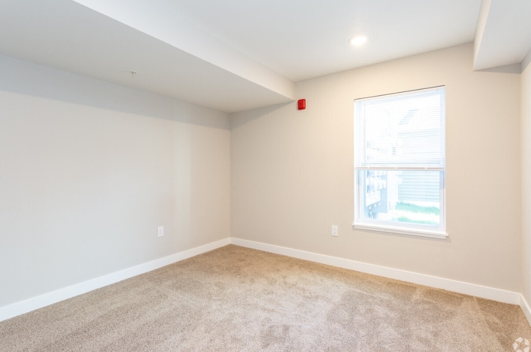 A room with a window and a red fire alarm on the wall.