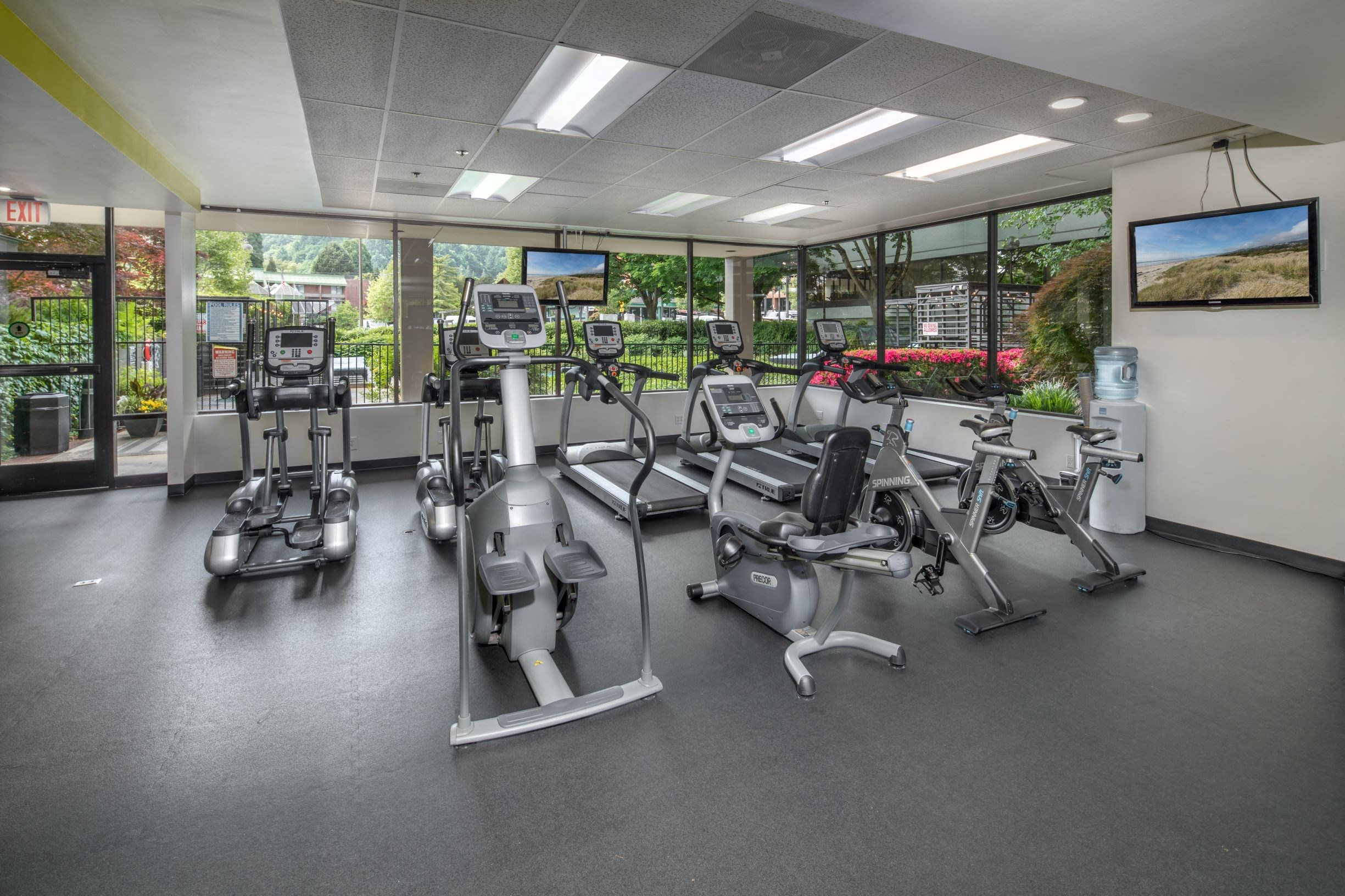 One-Bedroom Modern Apartments in Downtown Portland, OR - Linc 245 - Fitness Center with Rubber Matting, Cardio Equipment, Monitors, Water Dispenser, and Large Windows.
