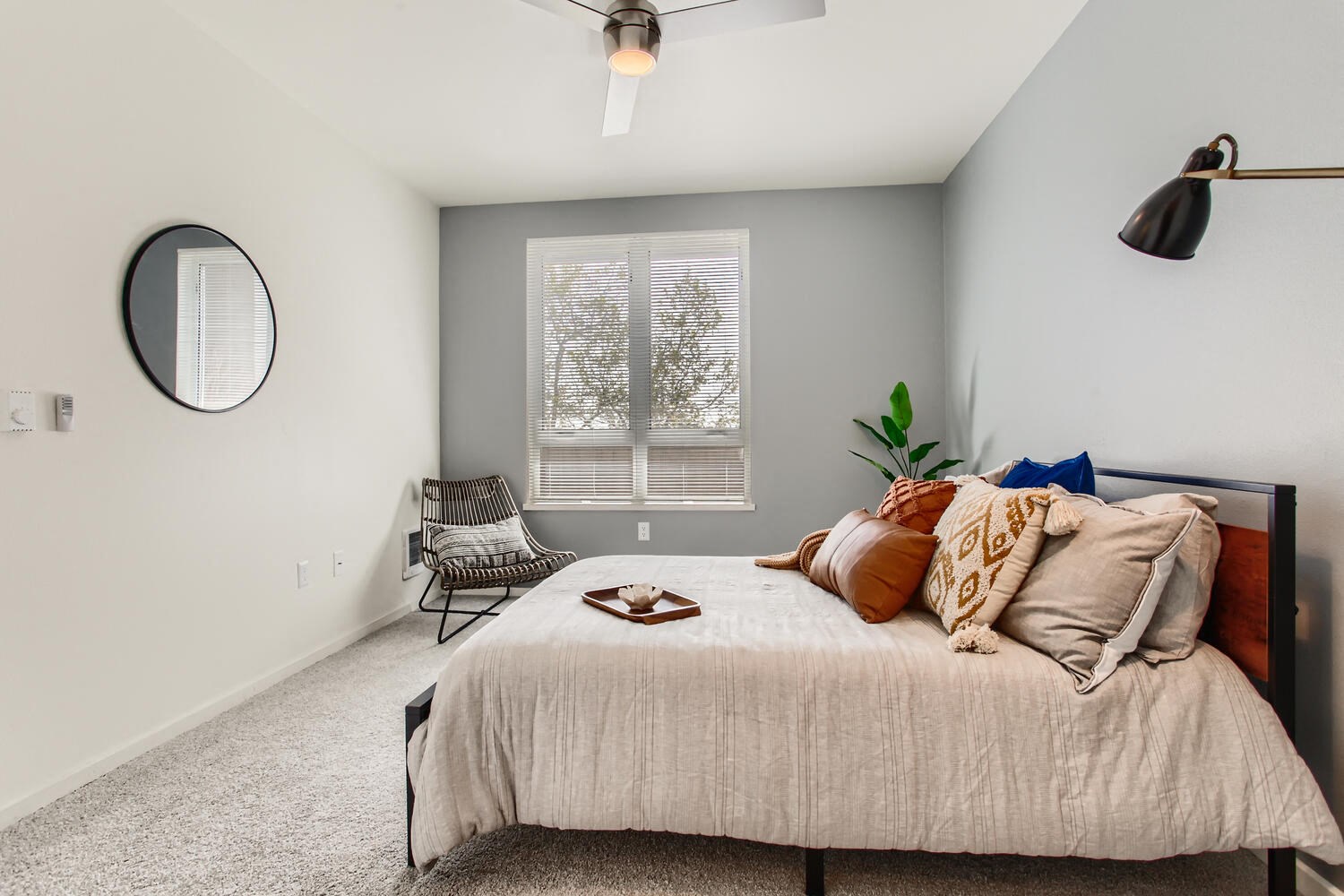 1-Bedroom Modern Apartments in Downtown Portland, OR - Linc 245 - Bedroom with Carpet Flooring, Large Bed, Mirror, Lamp, Chair, and Ceiling Fan.