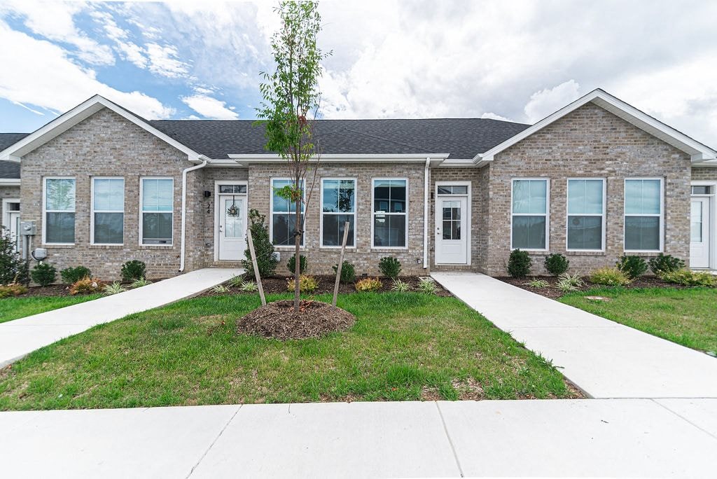 the front of a brick house with a lawn and sidewalk