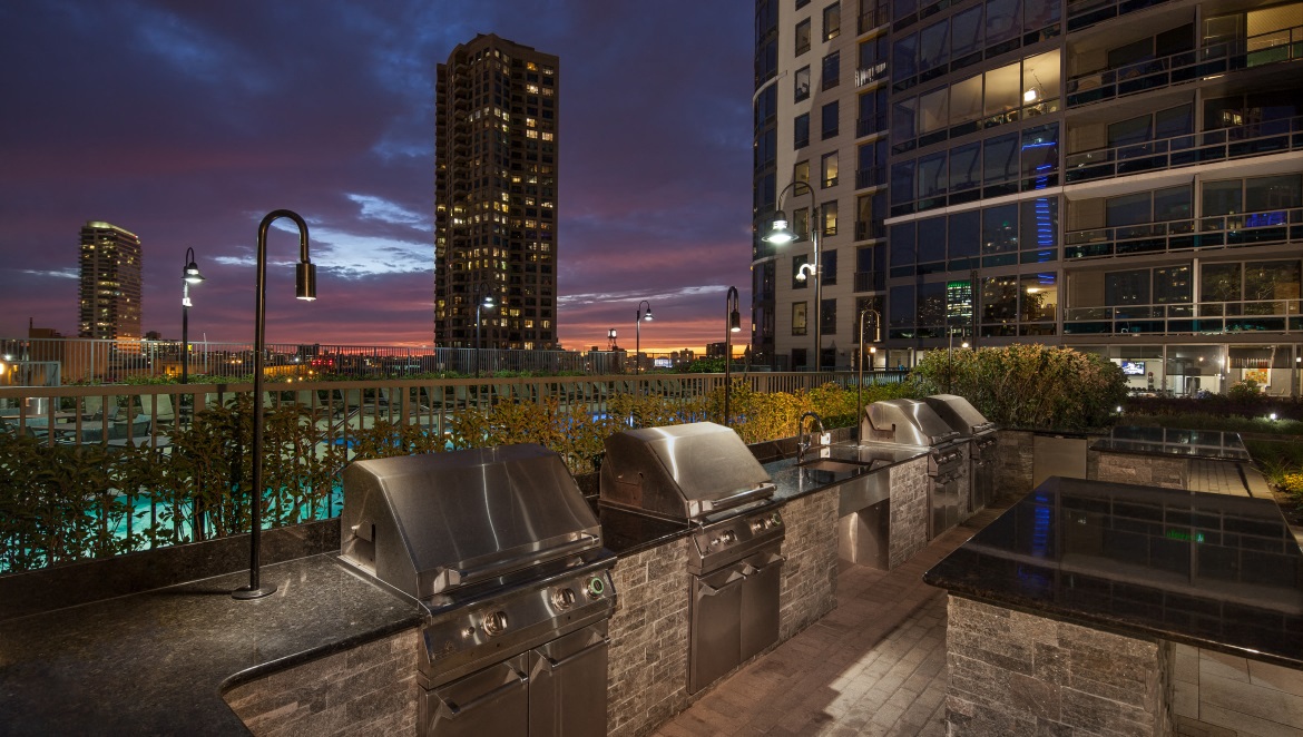 Outdoor grilling area at dusk with slight sunset and Kingsbury Plaza facade in the background