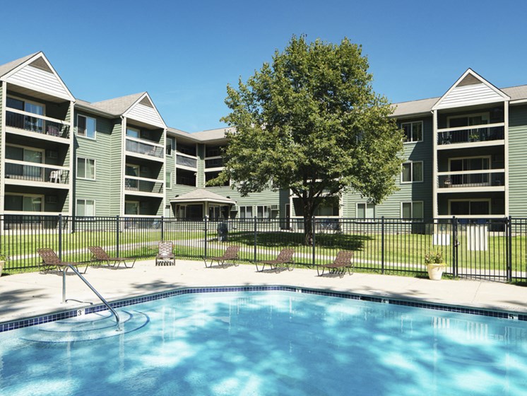 Outdoor pool with lounge chairs, surrounded by a black fence with the apartment building in the background