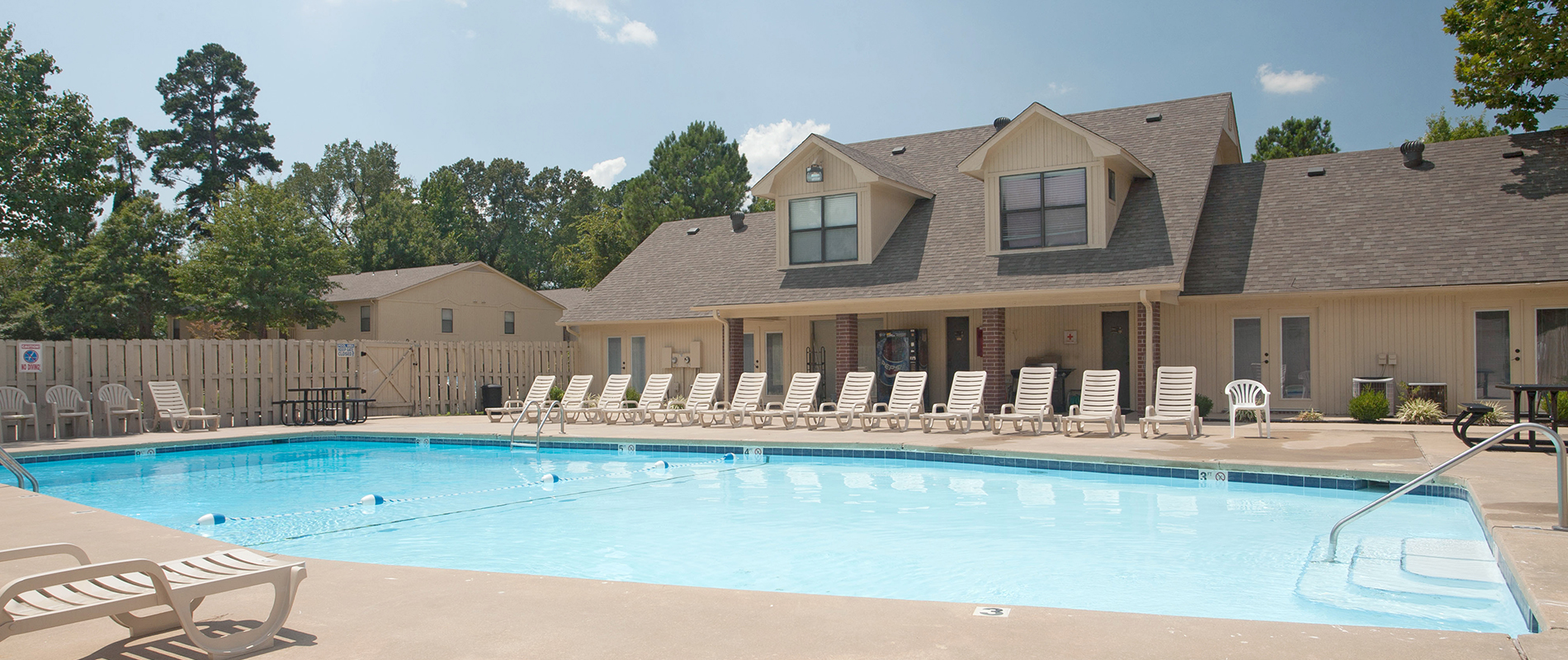 A large swimming pool surrounded by sun loungers in front of a building.