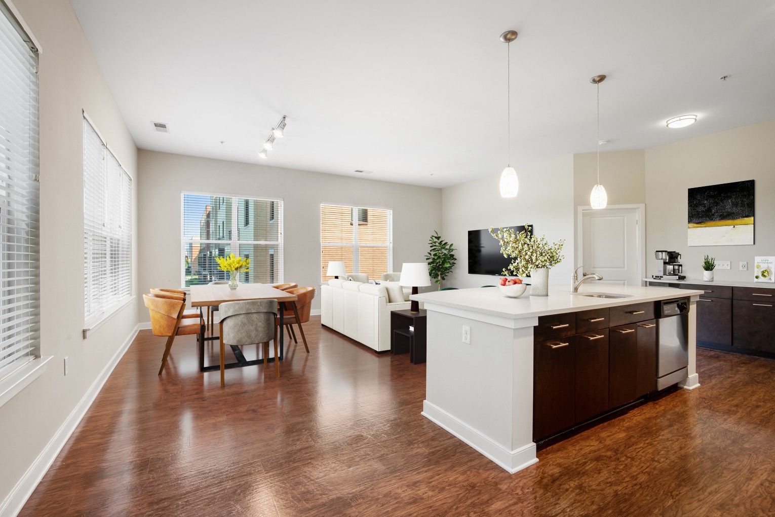 Modern open-concept apartment kitchen and living area featuring a large white kitchen island with barstools, polished flooring, and bright pendant lighting