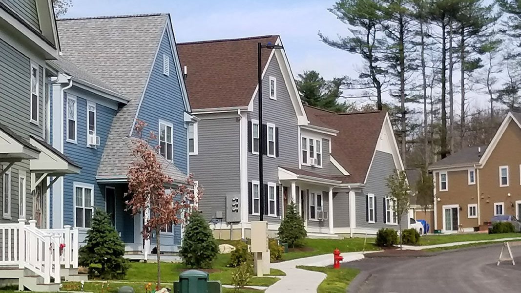 Street view of Greenridge Commons. Colorful homes with covered entries, nice green landscaping, woods behind.