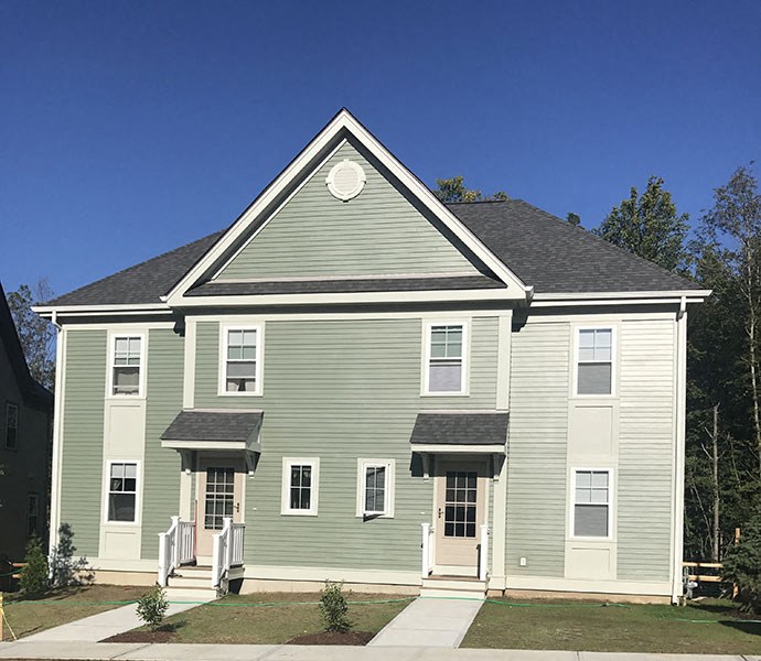 Large green duplex with covered entries and bushes in front, trees behind.