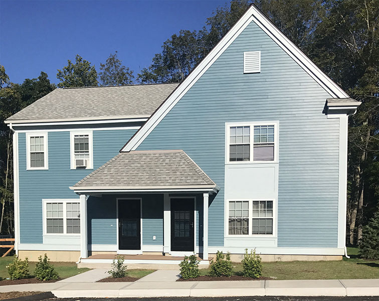 New blue house with covered entries and bushes in front.