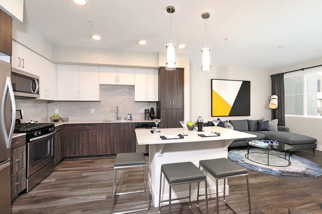 Modern kitchen with a stylish island, high bar stools, stainless steel appliances, and art on the wall, with a view into the living room.