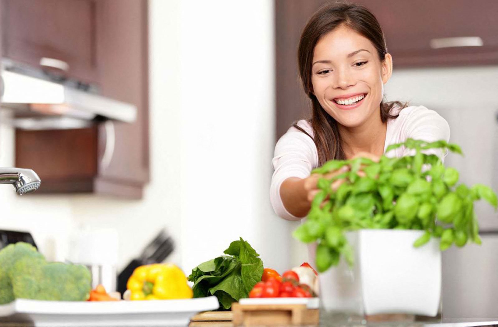 A woman is smiling while holding a bunch of green plants in a kitchen at The Helix in Denver, CO