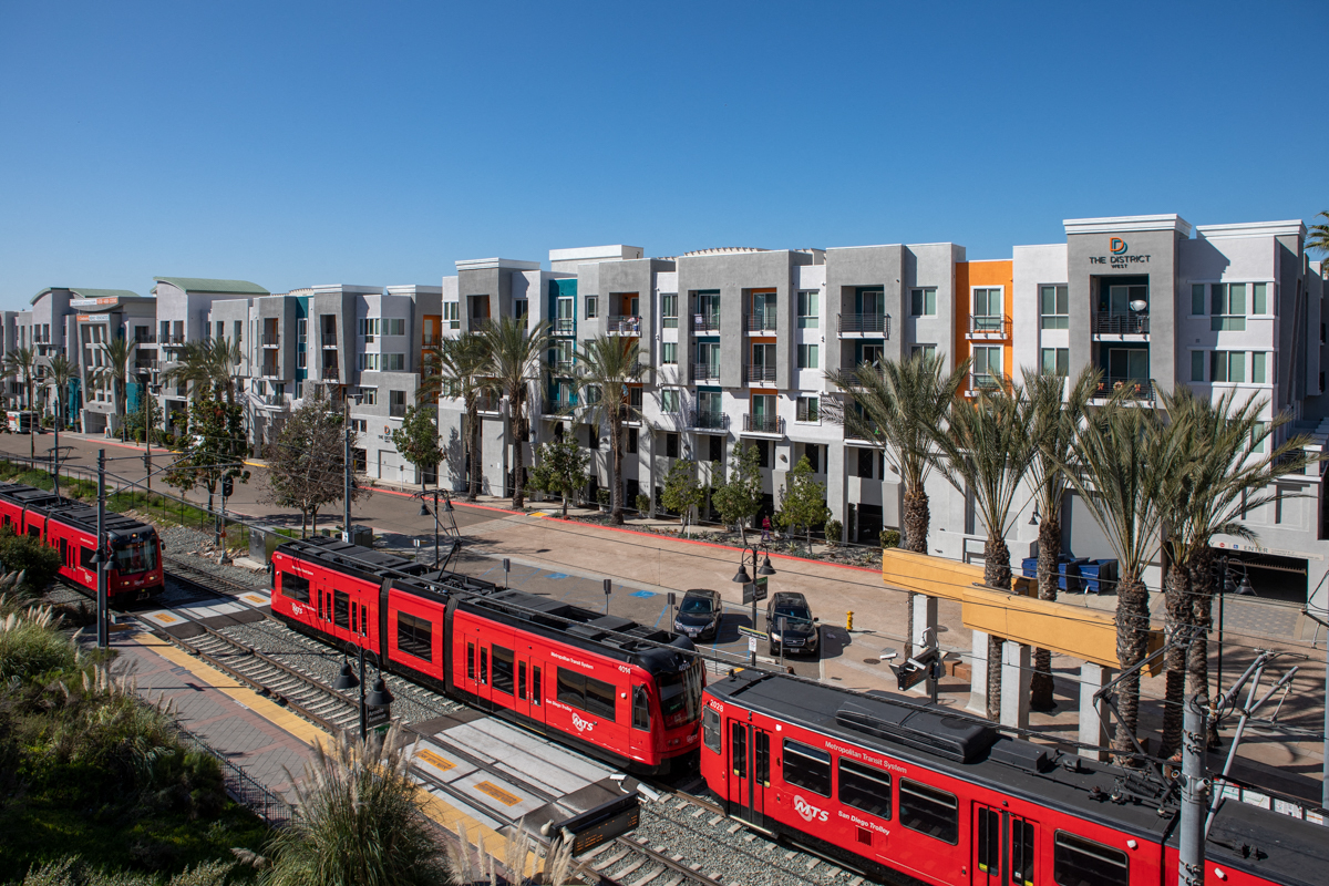 Dog-Friendly Apartments in La Mesa, CA - The District - Building Exterior with Trains, Street Access, and Palm Trees