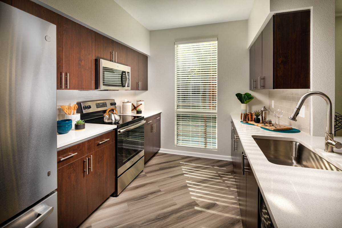 2-Bedroom Apartments in La Mesa, CA - The District - A Kitchen with Dark Wood Cabinetry, White Countertops, and Stainless Steel Appliances.
