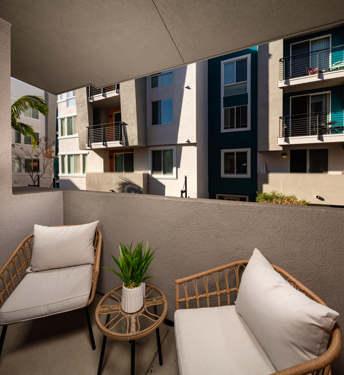 Pet-Friendly Apartments in La Mesa, CA - The District - Patio with Outdoor Furniture, View of Apartments Complex, and Trees