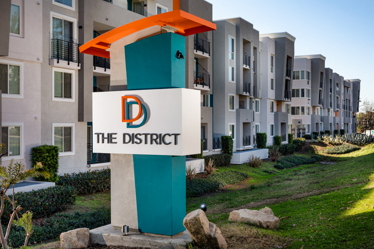 One-Bedroom Apartments in La Mesa, CA - The District - A Modern Apartment Community Exterior with a Large Property Entrance Sign and Landscaped Greenery.