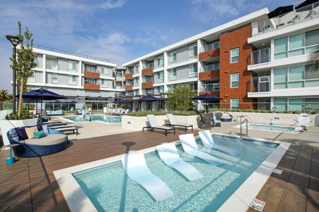 Resort-style pool deck with cabanas, lounge seating, and contemporary architecture at One Uptown Newport